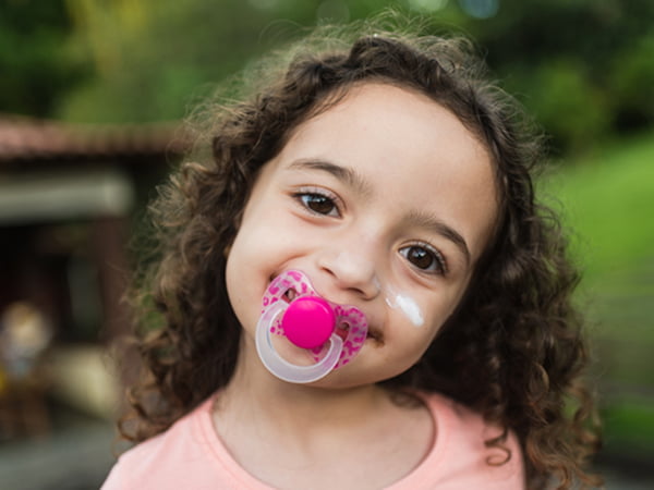 A little girl with a pacifier resting on her face, looking playful and curious