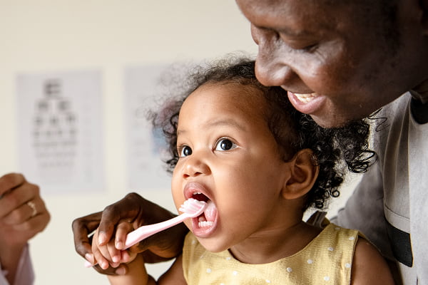 A man gently brush the teeth of a smiling baby in a bright bathroom setting