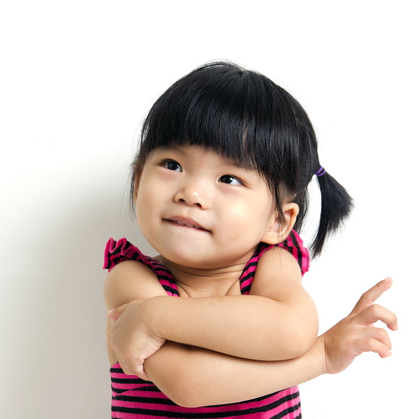 A little girl stands with her arms crossed, displaying a thoughtful expression on her face