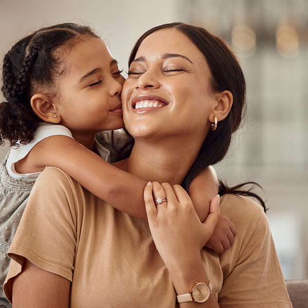 A woman and her daughter embrace, both smiling joyfully in a warm, affectionate moment