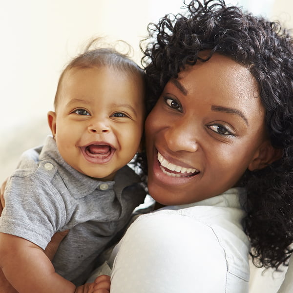 A woman smiles while holding a baby in her arms, radiating warmth and joy