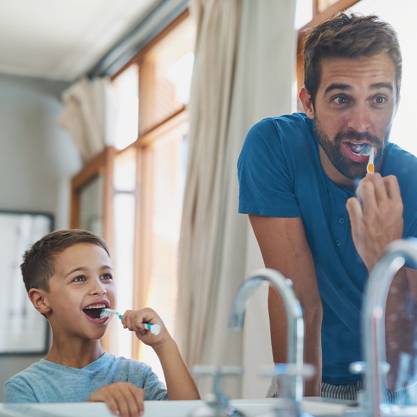 A man and a boy are brushing their teeth together in a bathroom, promoting good dental hygiene