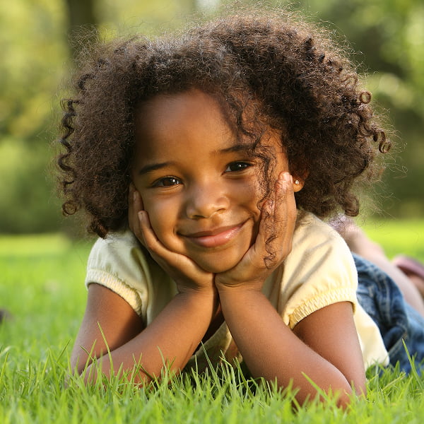 A young girl lies on the grass in a park, enjoying a sunny day surrounded by greenery