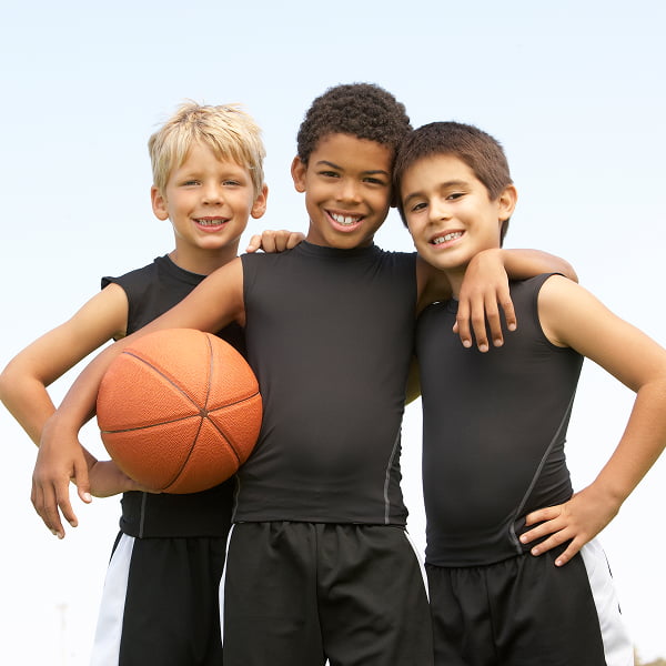 Three boys in black shirts and shorts are holding a basketball, ready to play in an outdoor setting