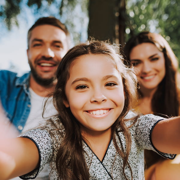 A family of four smiling together while taking a selfie outdoors