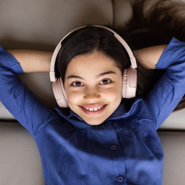 A girl with headphones relaxing on a couch, enjoying music or a podcast in a cozy setting
