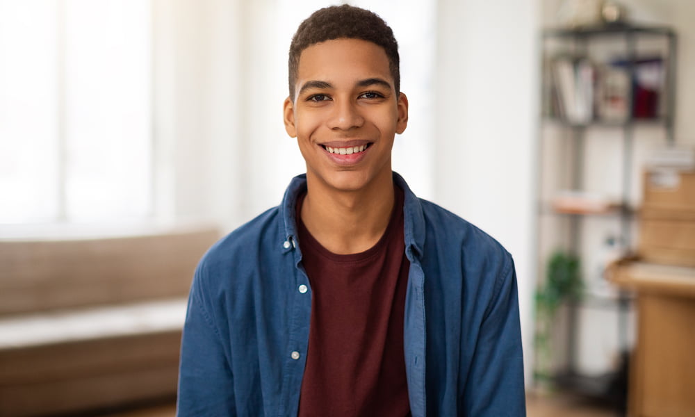 A young man smiles warmly while sitting in his cozy living room, surrounded by comfortable furniture and soft lighting