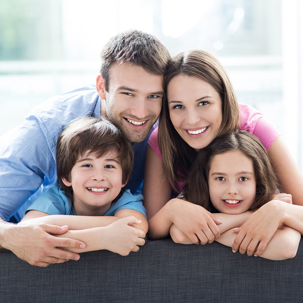 A family of four smiles together while posing on a cozy couch in a warmly lit living room
