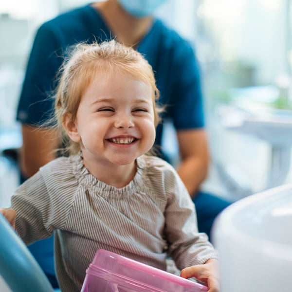 A young girl sitting in a dentist chair, looking around with curiosity in a bright dental office