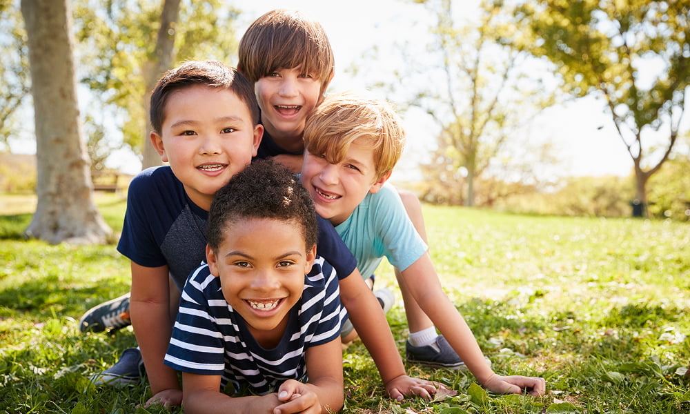 Four smiling children are lying on the grass, enjoying a sunny day together