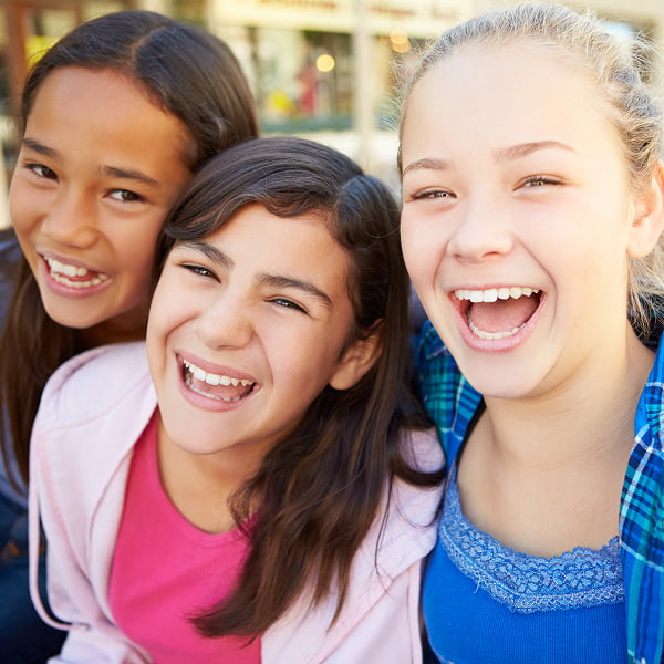 Three girls joyfully laughing and smiling together, showcasing a moment of friendship and happiness