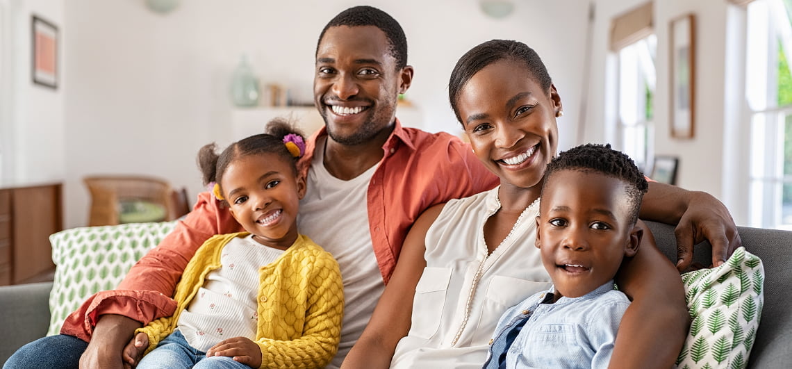 A family of four sitting closely together on a couch, smiling and enjoying each other's company in a cozy living room
