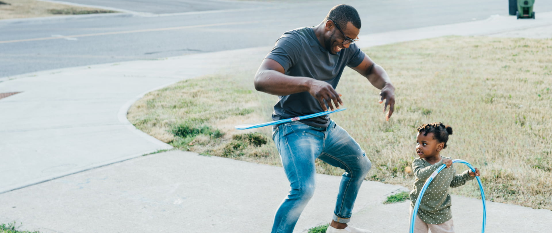 A man and a child joyfully playing together with a colorful hula hoop in a sunny outdoor setting